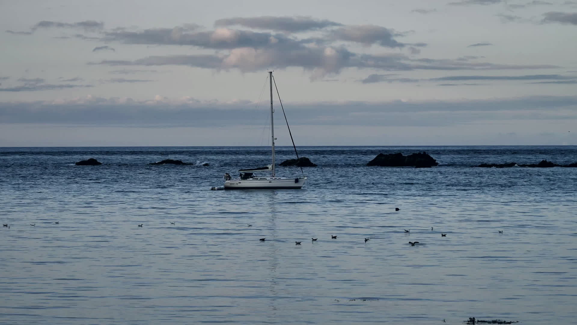 A sailboat at anchor near rocks on a grey day