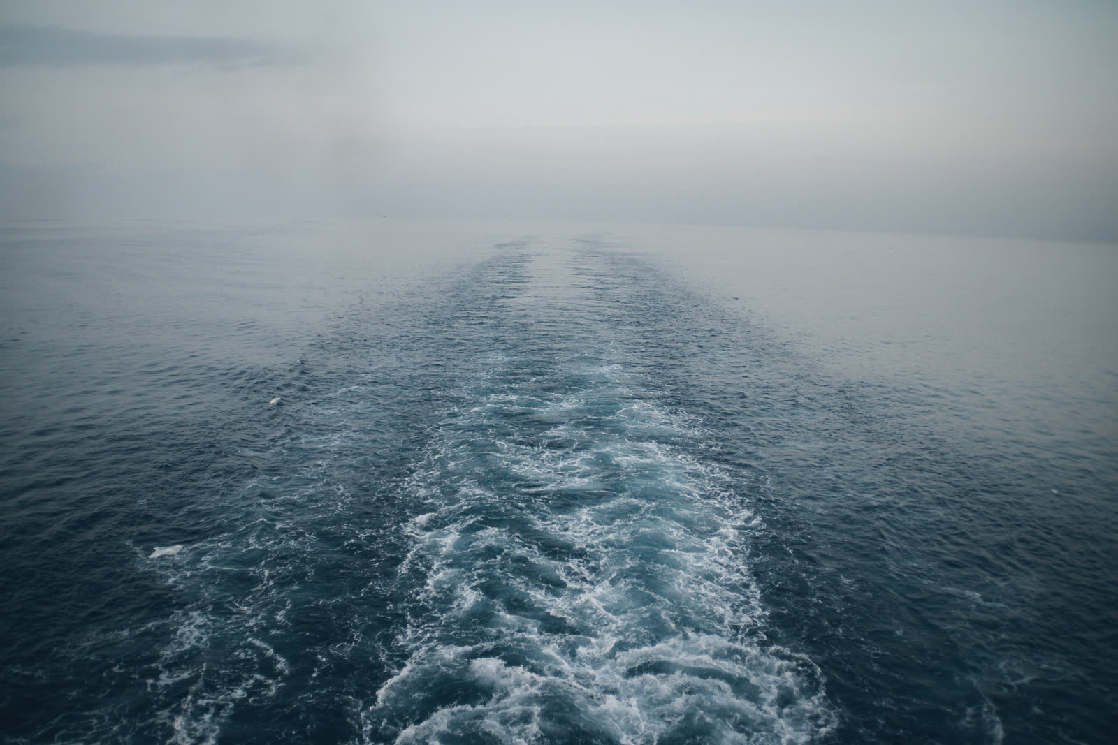 A boat's wake running into fog on a grey sea